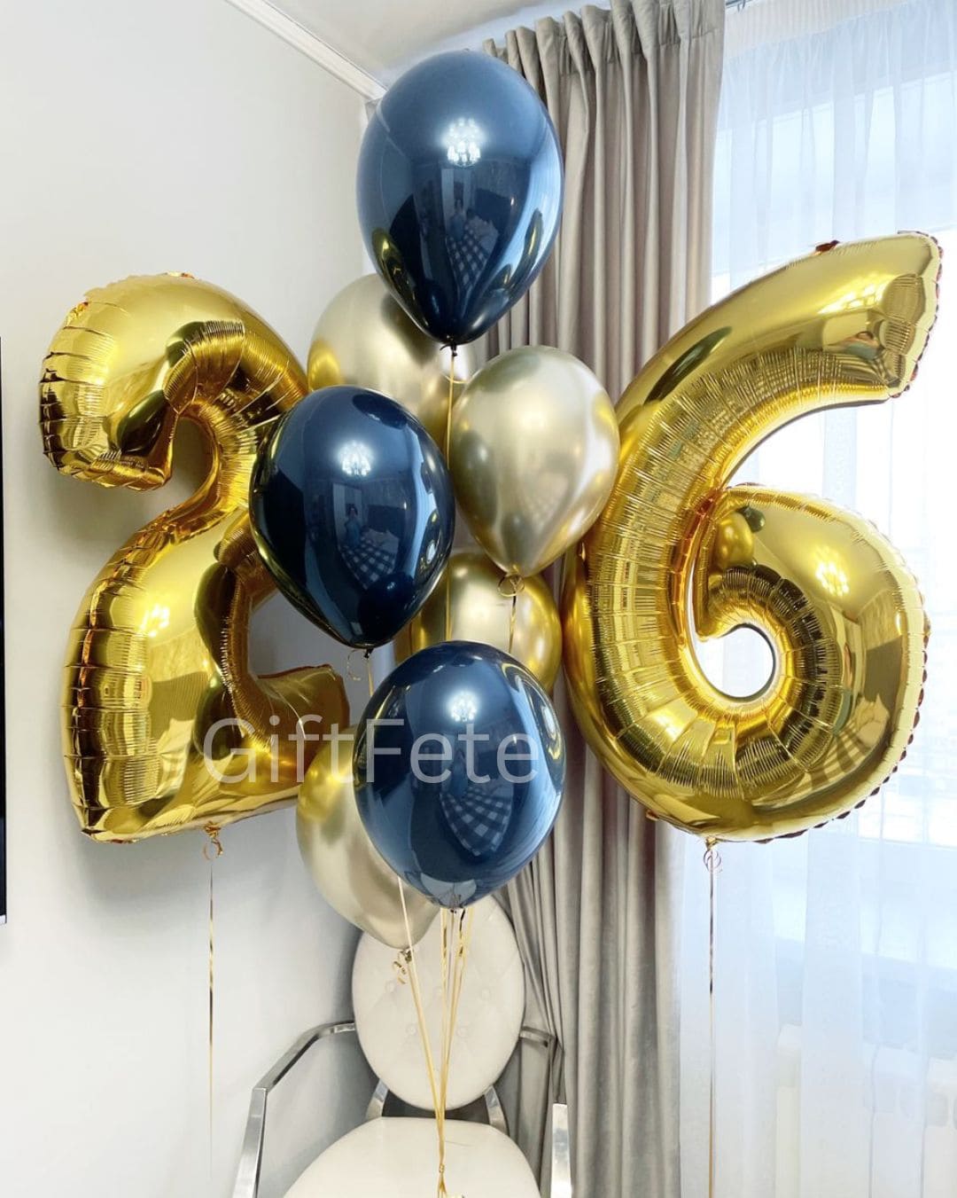 Gold and blue foil balloons shaped like the number 26 against a white wall.