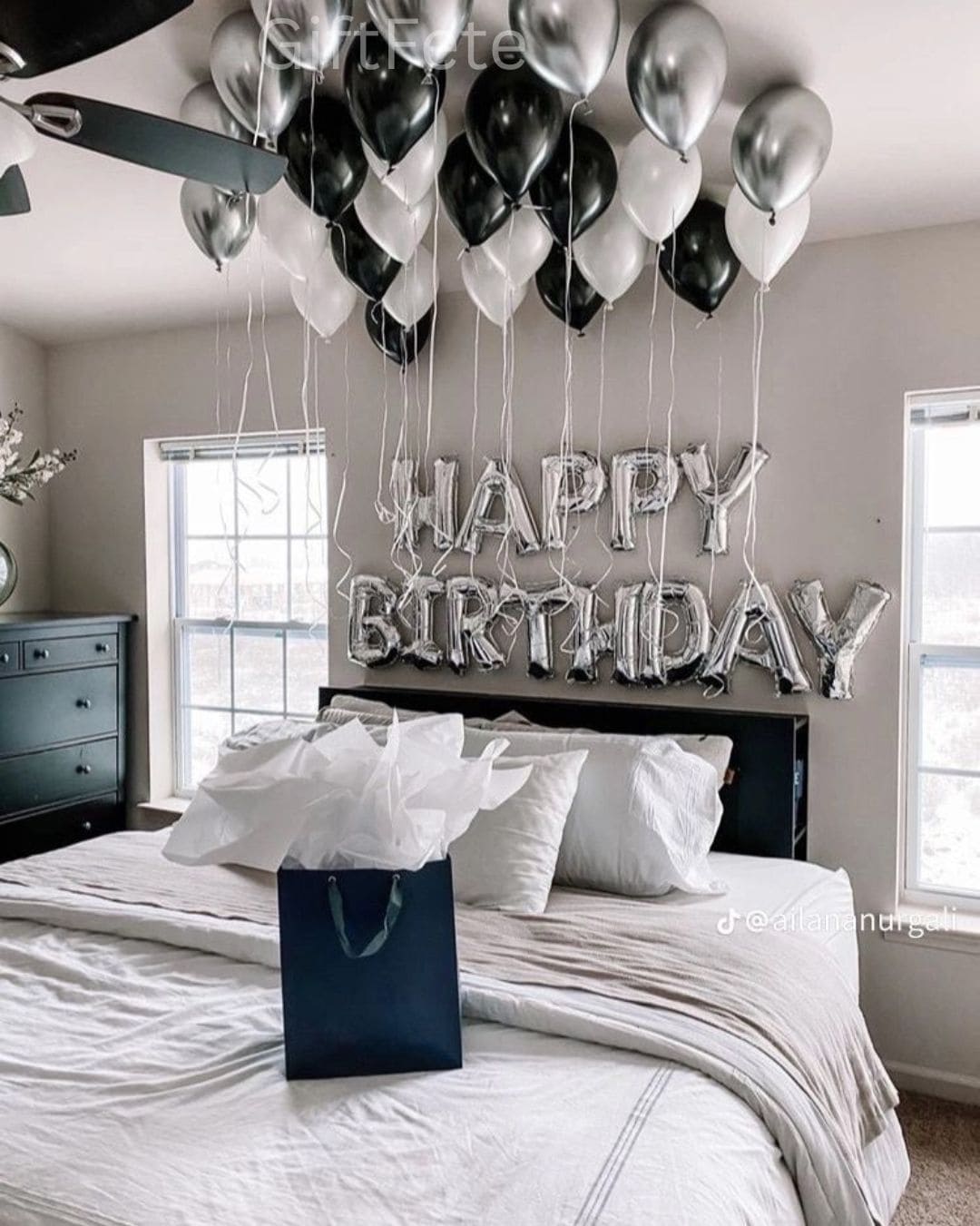 Bedroom with 'Happy Birthday' balloons and a gift bag on the bed.