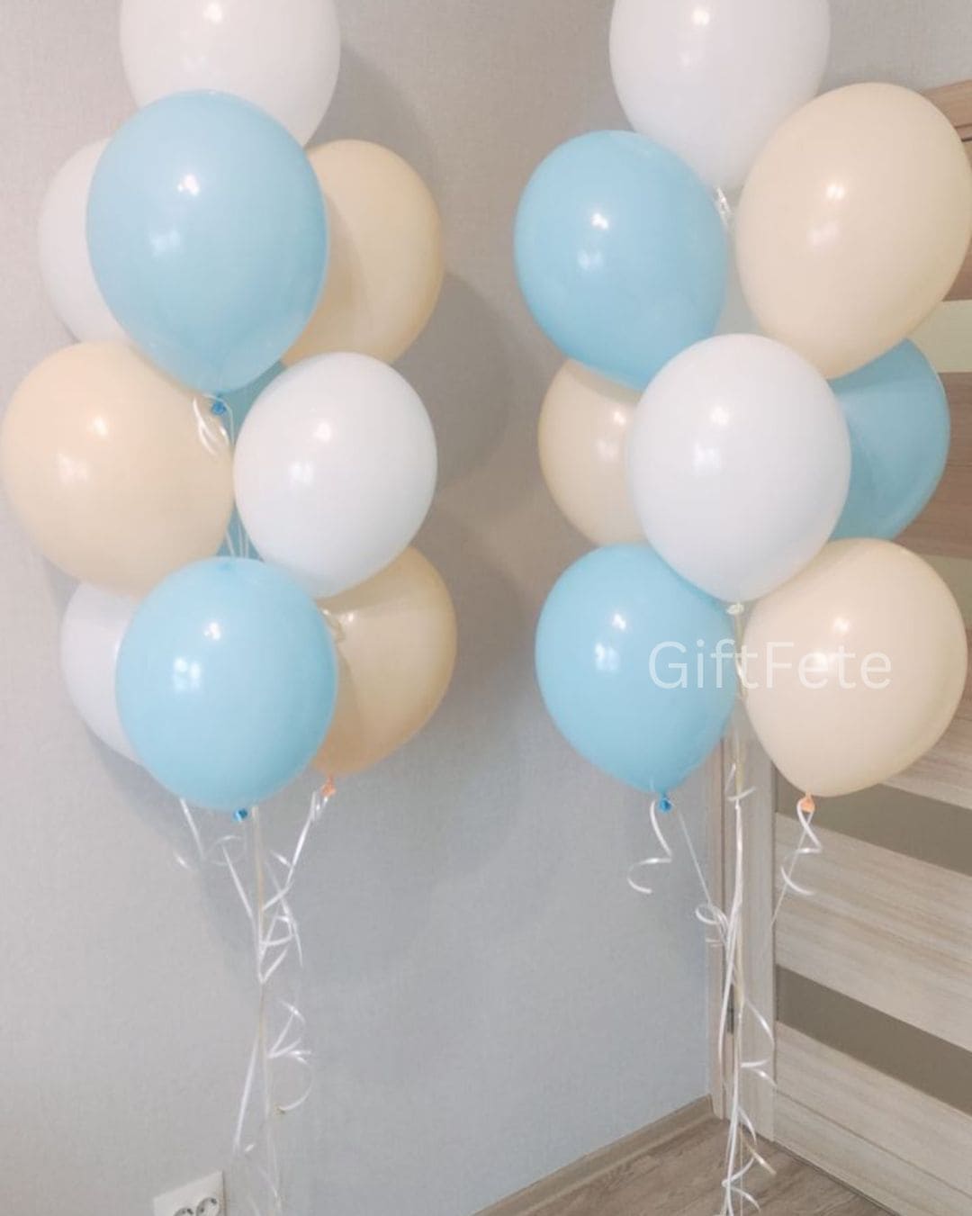 Balloon arch with blue, white, and beige balloons against a neutral wall.