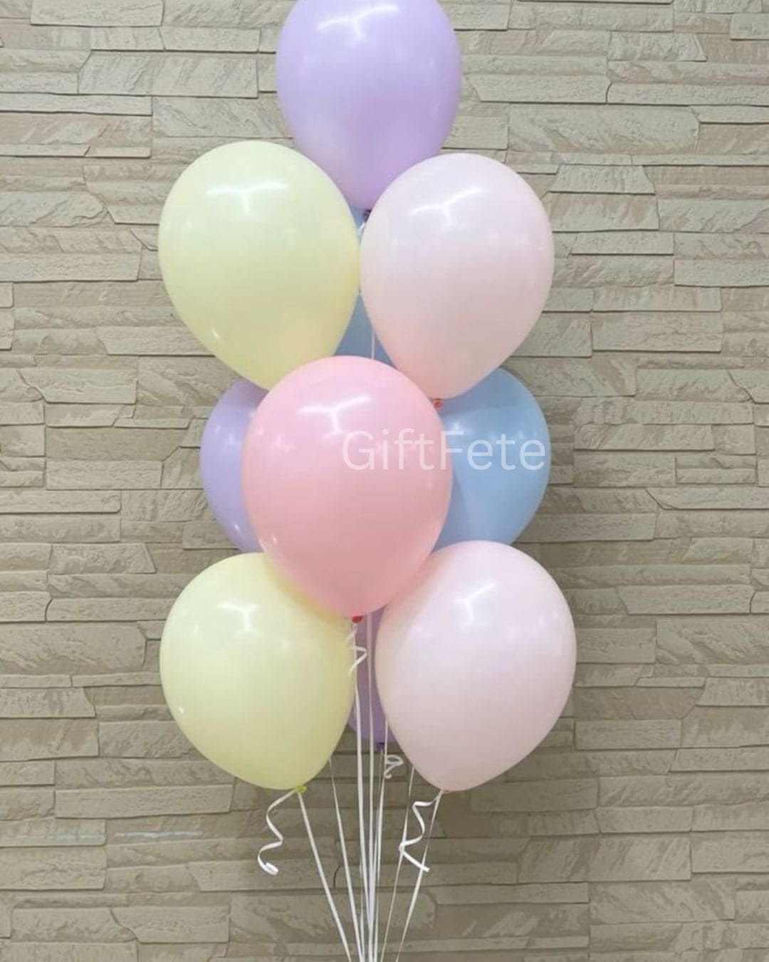 Bouquet of pastel-colored balloons against a stone wall background with 'GiftFete' branding.