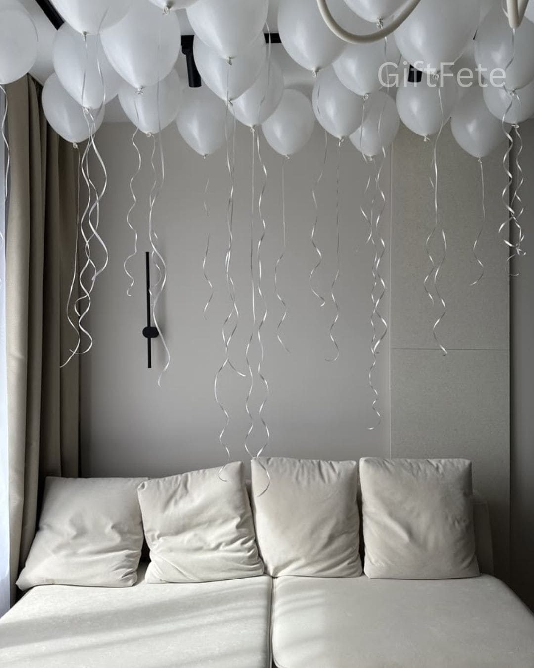White balloons and ribbons hanging above a bed with 'GiftFete' branding.